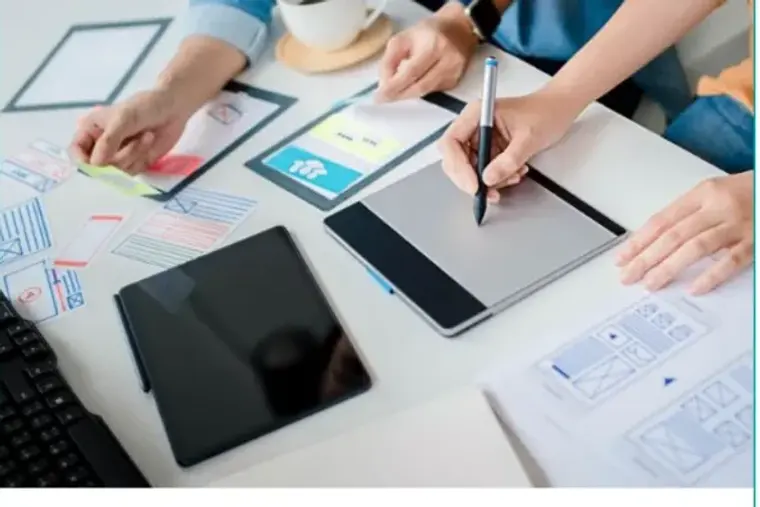 Two people sketching layouts on paper beside a tablet